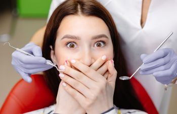 A terrified woman suffering from dentophobia covering her mouth with both hands during a dental appointment.