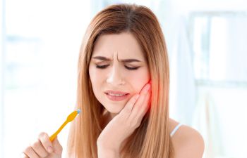 Woman with a toothbrush feeling severe toothache due to cavities.