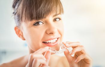 A woman with perfect teeth holding an invisalign aligner.